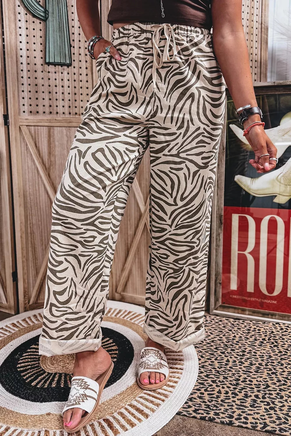 Full-length zebra print wide leg pants with white slide sandals and a rug