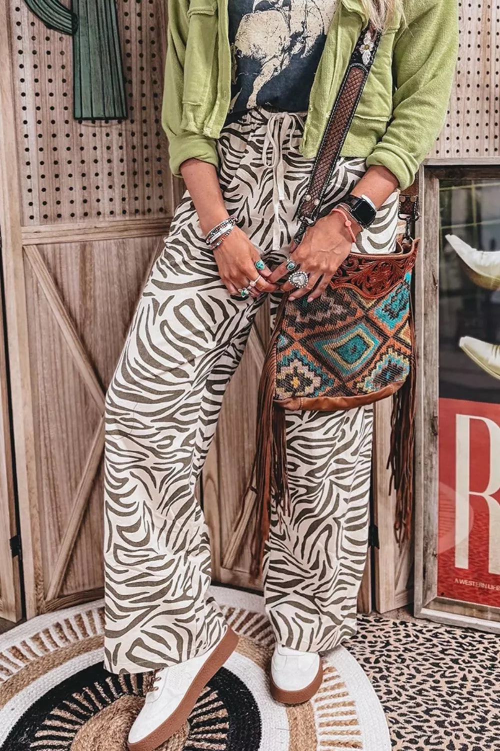 Zebra print wide leg pants styled with a green jacket and a woven shoulder bag