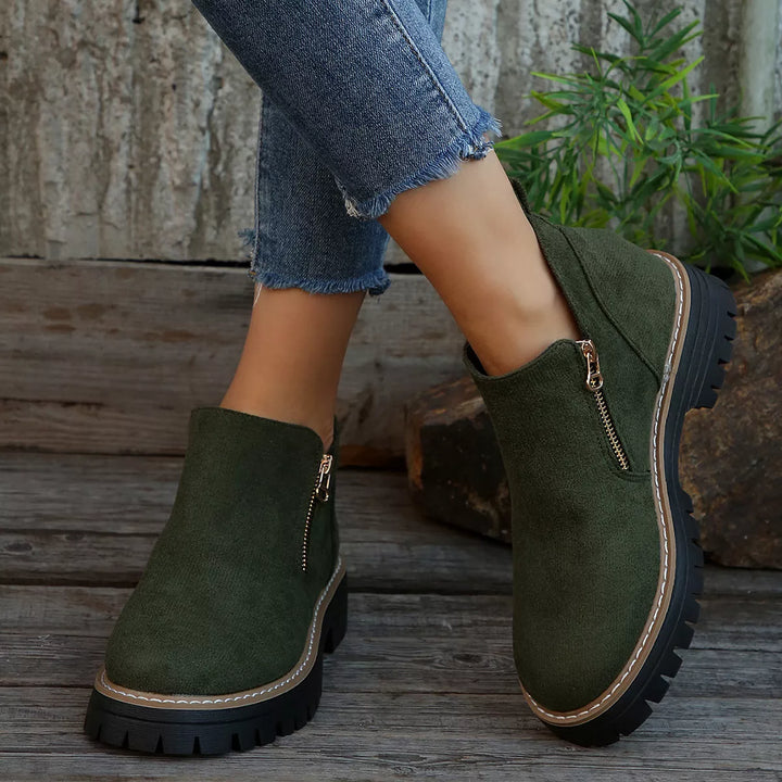 Olive green block heel ankle boots seen from the front on wooden planks