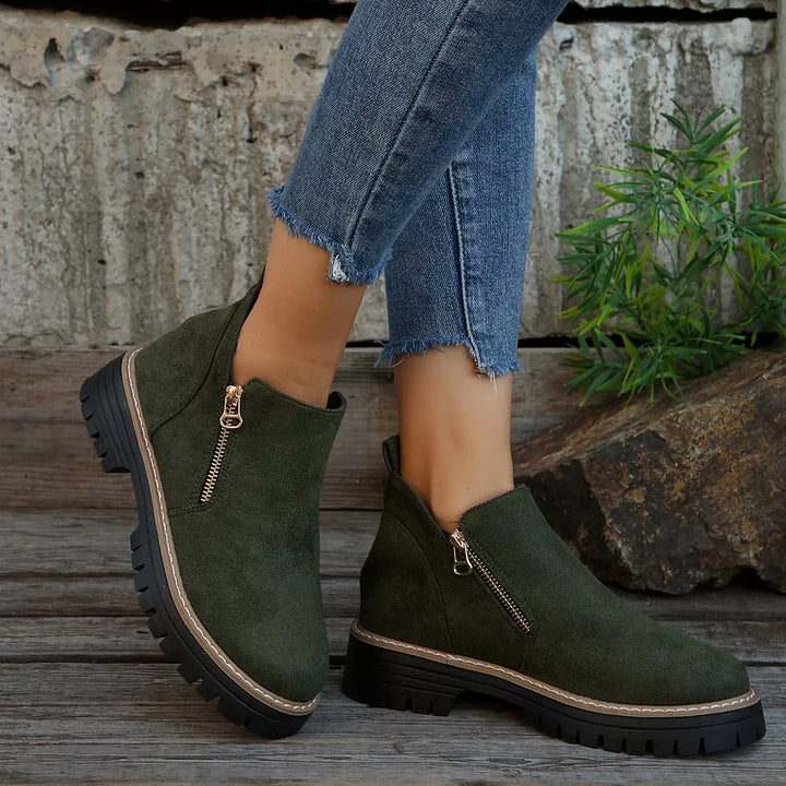 Women's ankle boots in olive green with chunky lug sole and side zipper, worn with jeans