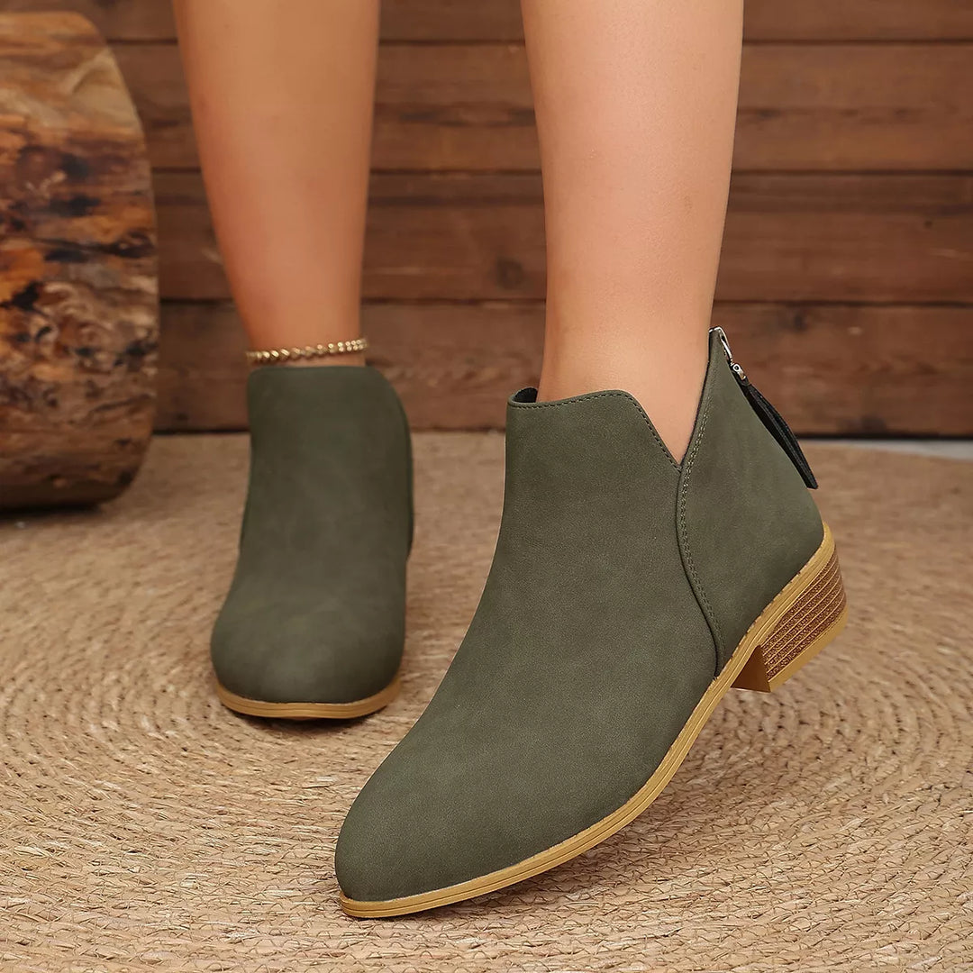 Olive V-cut ankle boots with a low block heel, front angle on a woven rug