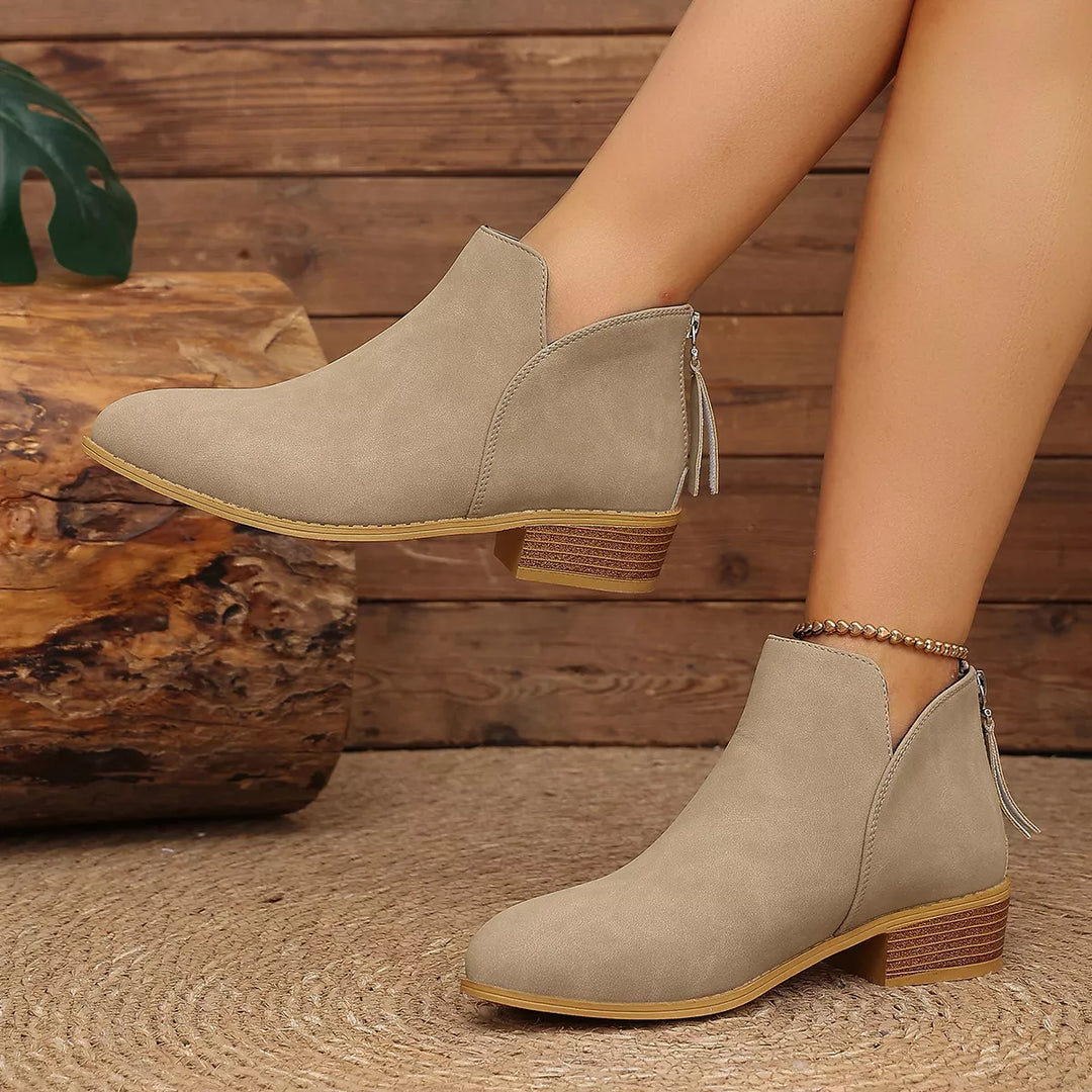 Taupe ankle boots worn with one foot raised, showing the V-cut front