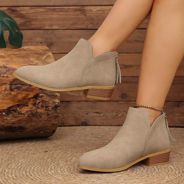 Taupe ankle boots worn with one foot raised, showing the V-cut front