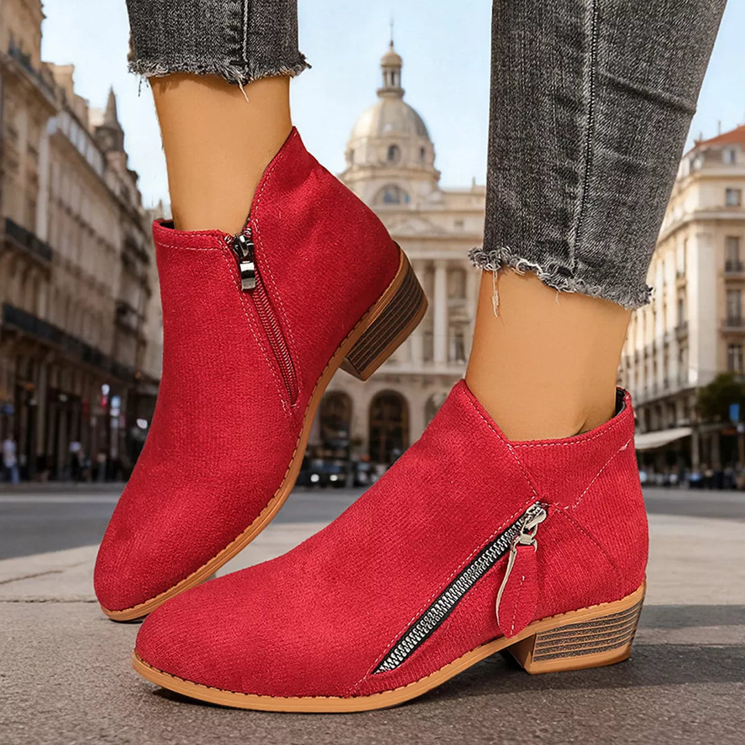 Red ankle boots with side zip and block heel, worn on a city street