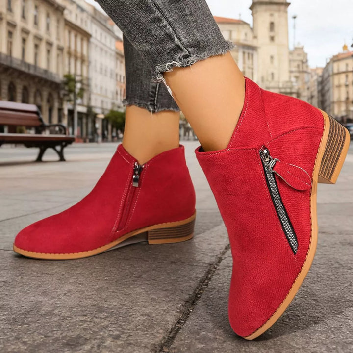 Red pointed toe ankle boots in a walking pose on cobblestones