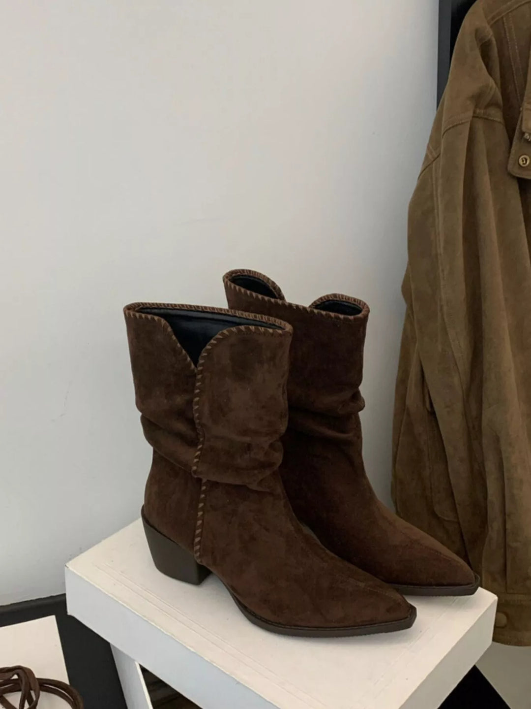 Dark brown slouchy ankle boots with block heel and stitched edge on a display stand
