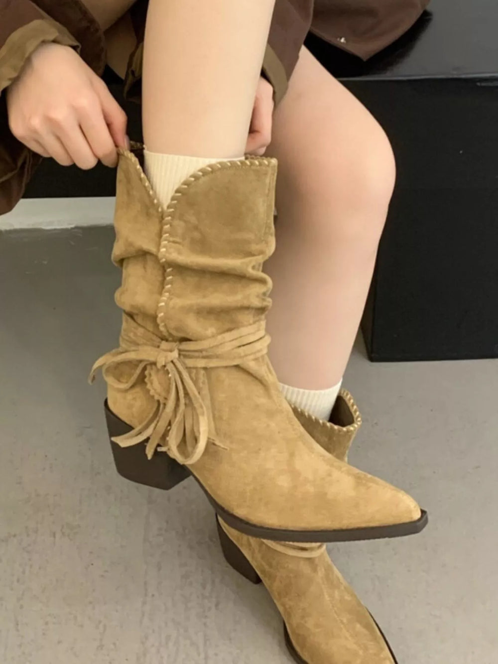 Tan slouchy ankle boot with fringe tie worn on foot, seated pose