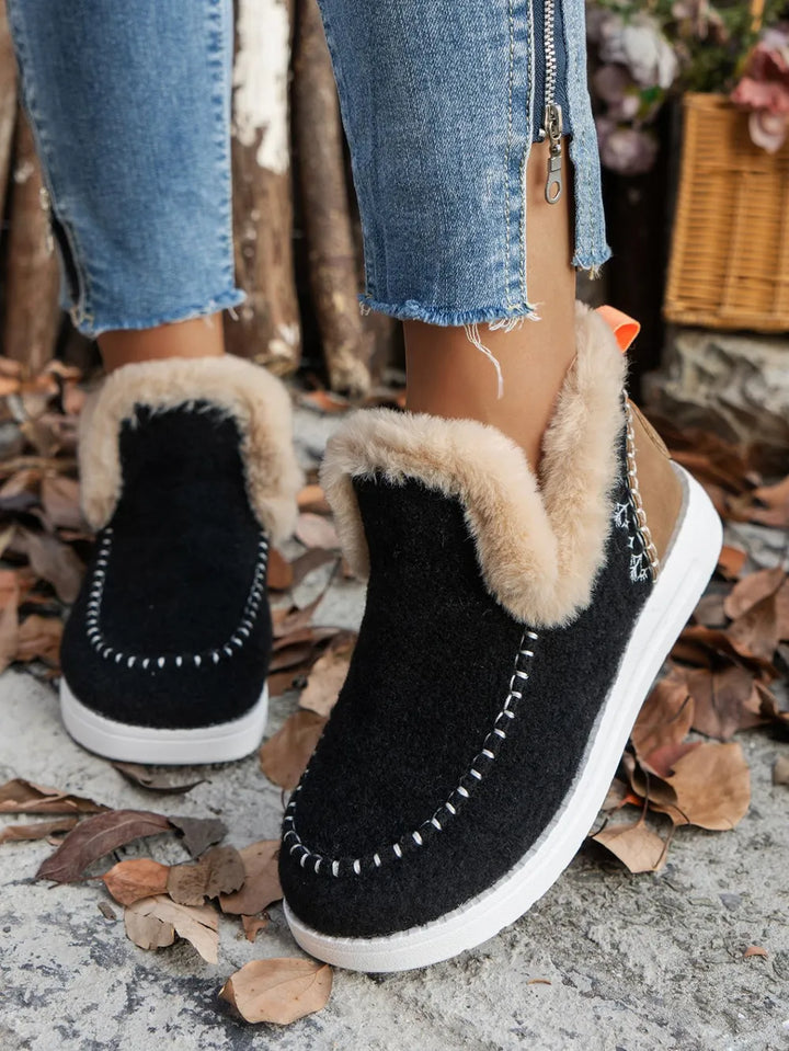 Black studded ankle boots with a fur-look cuff, worn over autumn leaves