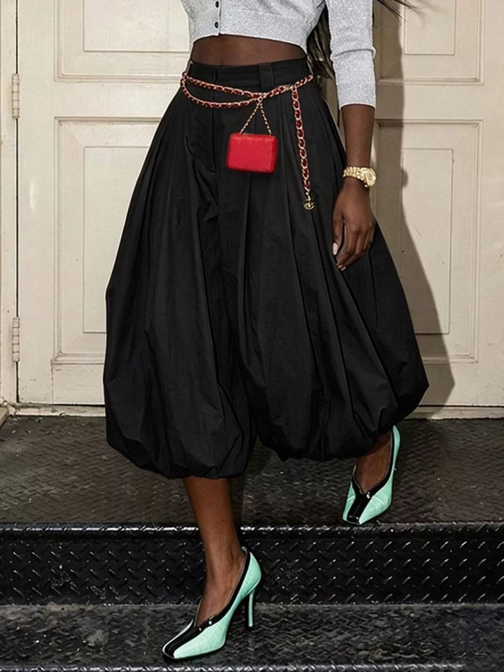 Black balloon pants with pleats, front view with a small red bag