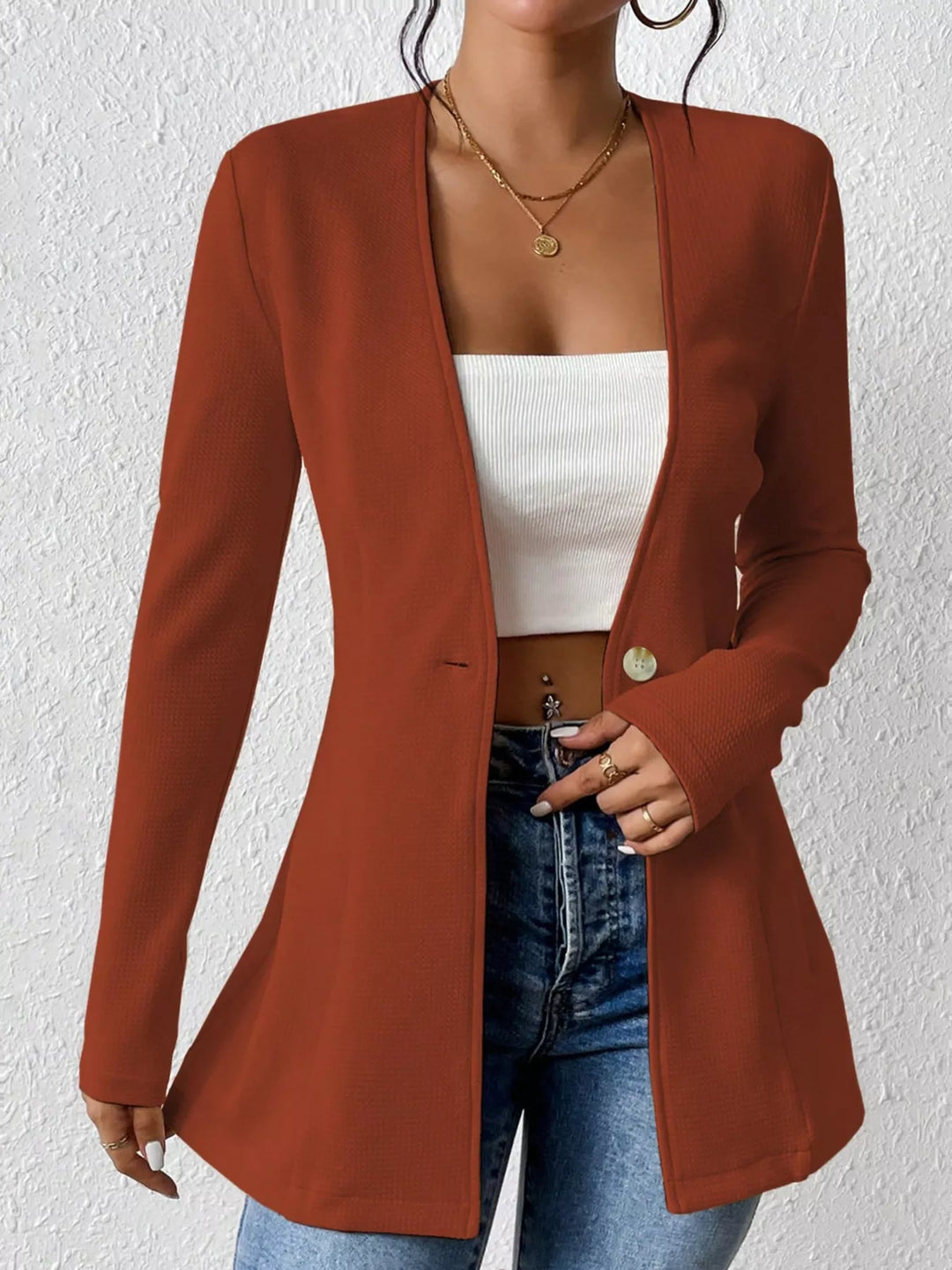 Rust collarless blazer worn open over a white crop top and jeans