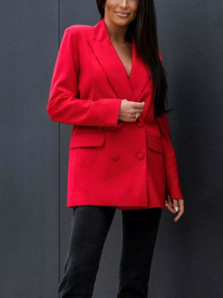 Red double breasted blazer buttoned, with black pants against a dark wall