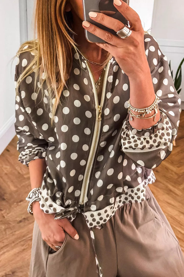 Taupe polka dot zip up jacket with a tied hem worn over beige pants