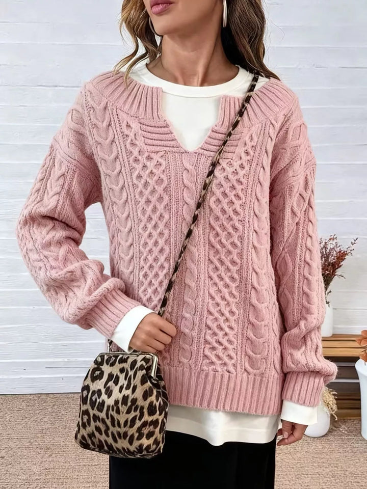 Pink cable knit sweater worn with black leggings, one hand in pocket