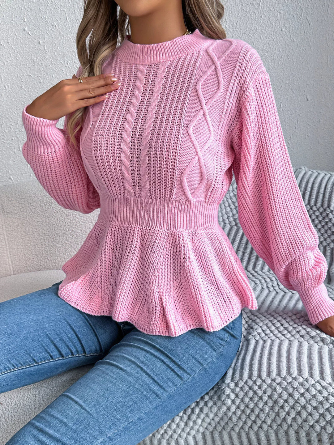 Pink crew neck sweater with ruffled peplum hem, model seated on a sofa