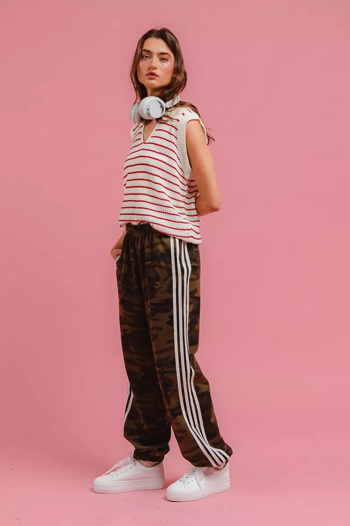 Left side view of camo track pants with striped top and white sneakers