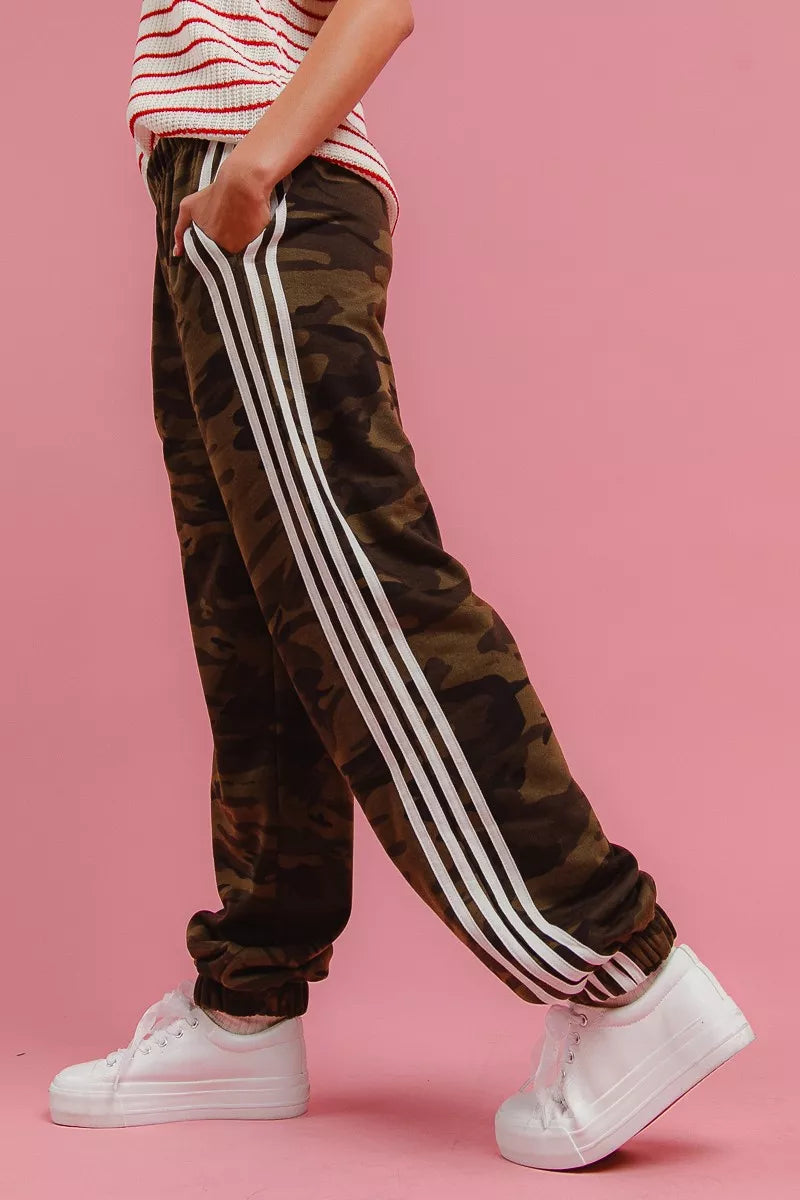 Camo track pants with white side stripes in a walking side view