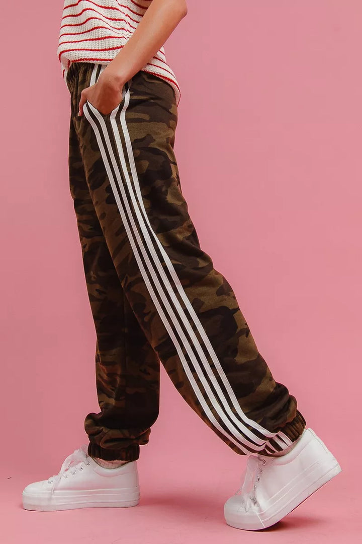 Camo track pants with white side stripes in a walking side view