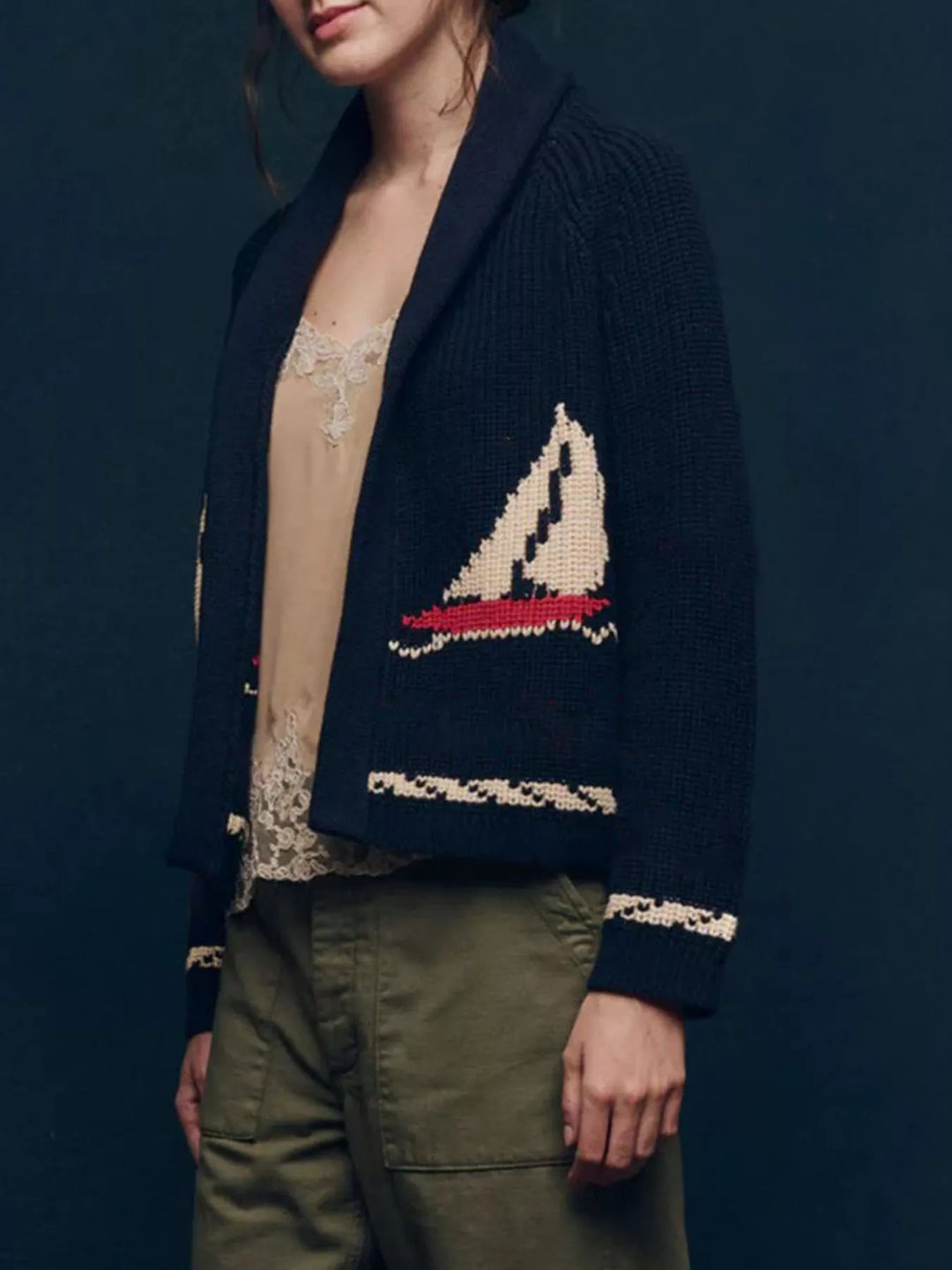 Navy chunky knit cardigan with sailboat pocket motif over a cami and green pants