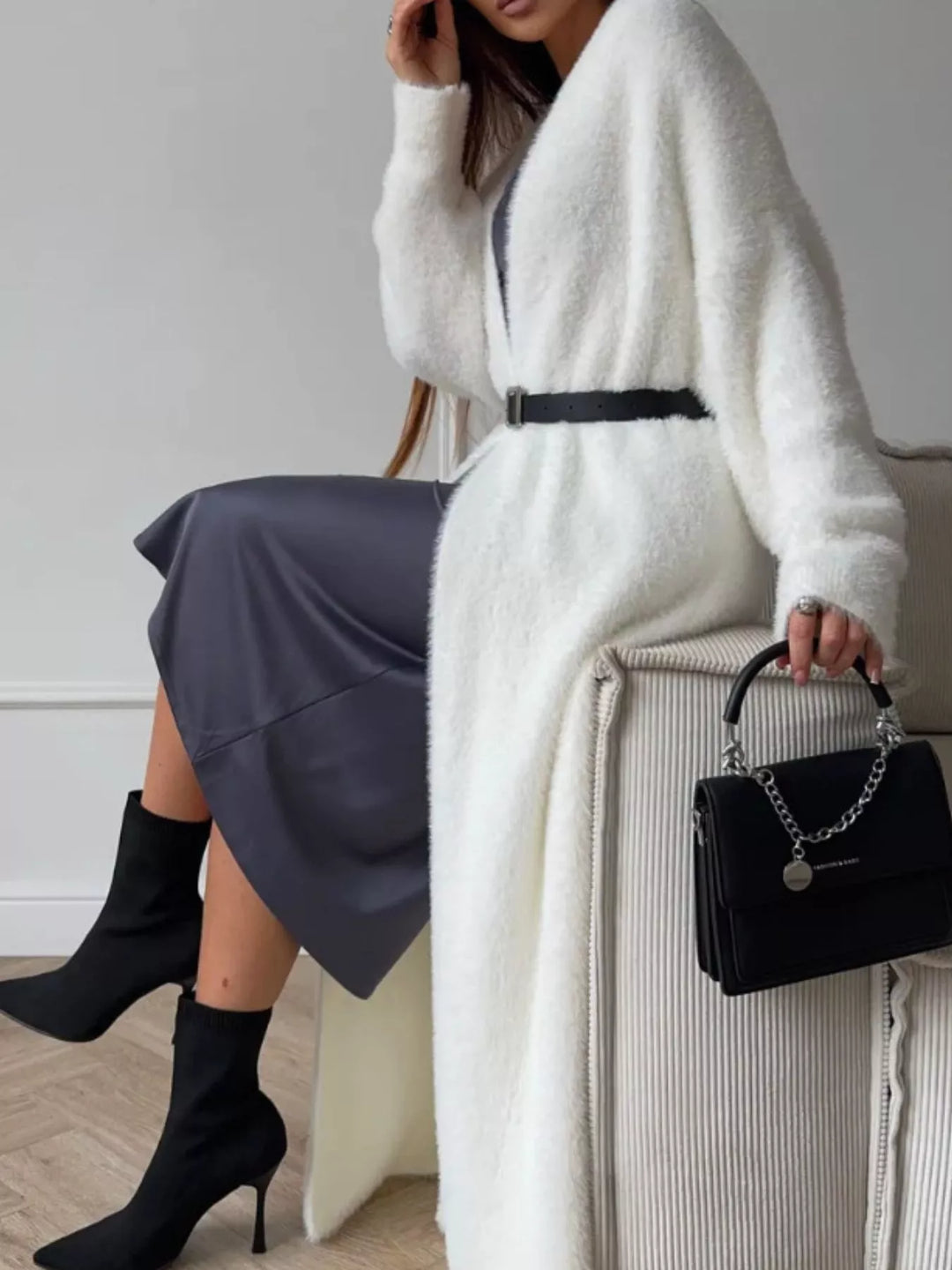 Ivory cardigan belted at the waist while seated, with a black handbag