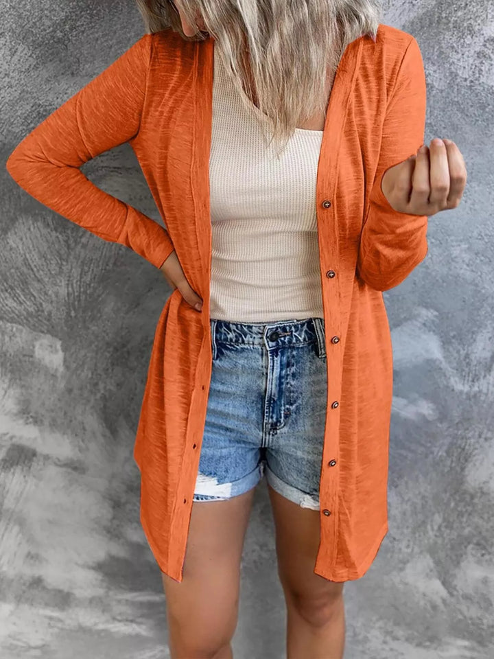 orange longline cardigan, one hand raised, worn with cuffed denim shorts