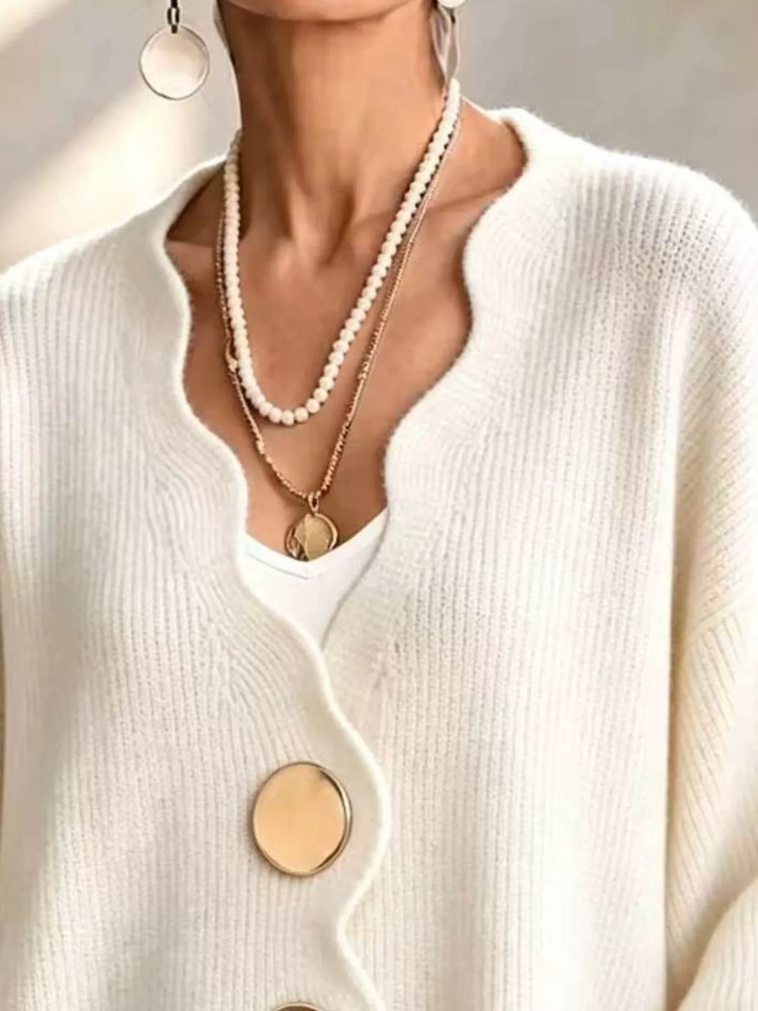 Close-up of the cream cardigan wavy neckline layered with pearl necklaces