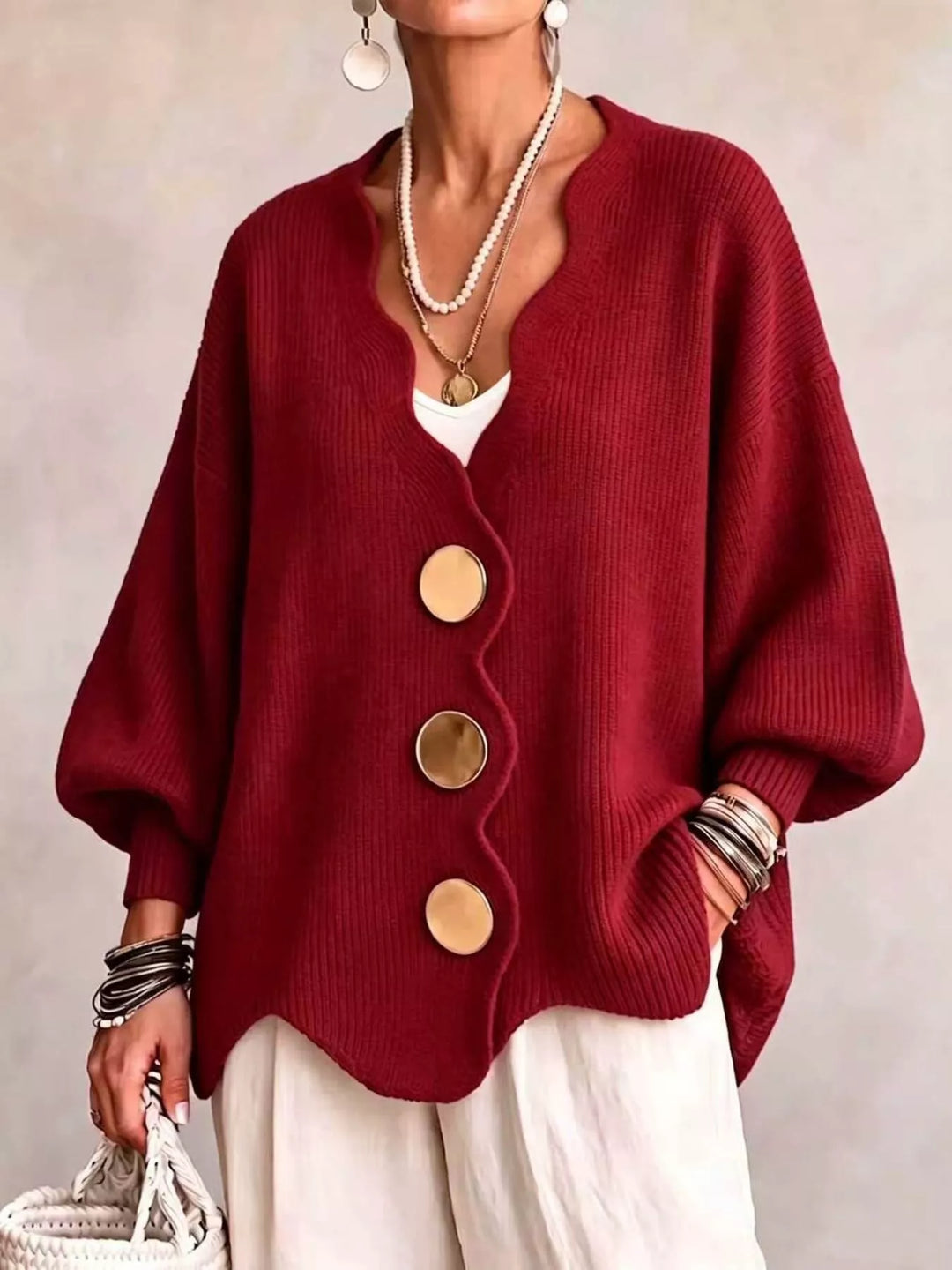 Oversized scalloped edge cardigan in red with gold buttons, worn over white pants