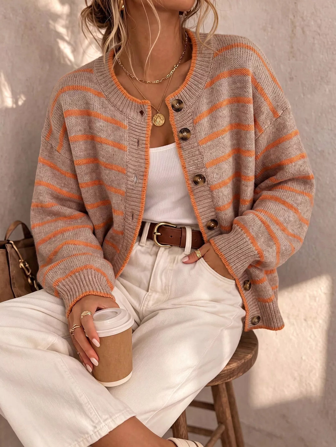 Camel striped button front cardigan worn with white pants and a brown belt