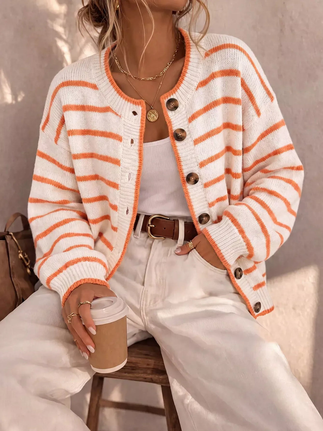 Ivory cardigan with orange stripes and button front, seated with a coffee cup
