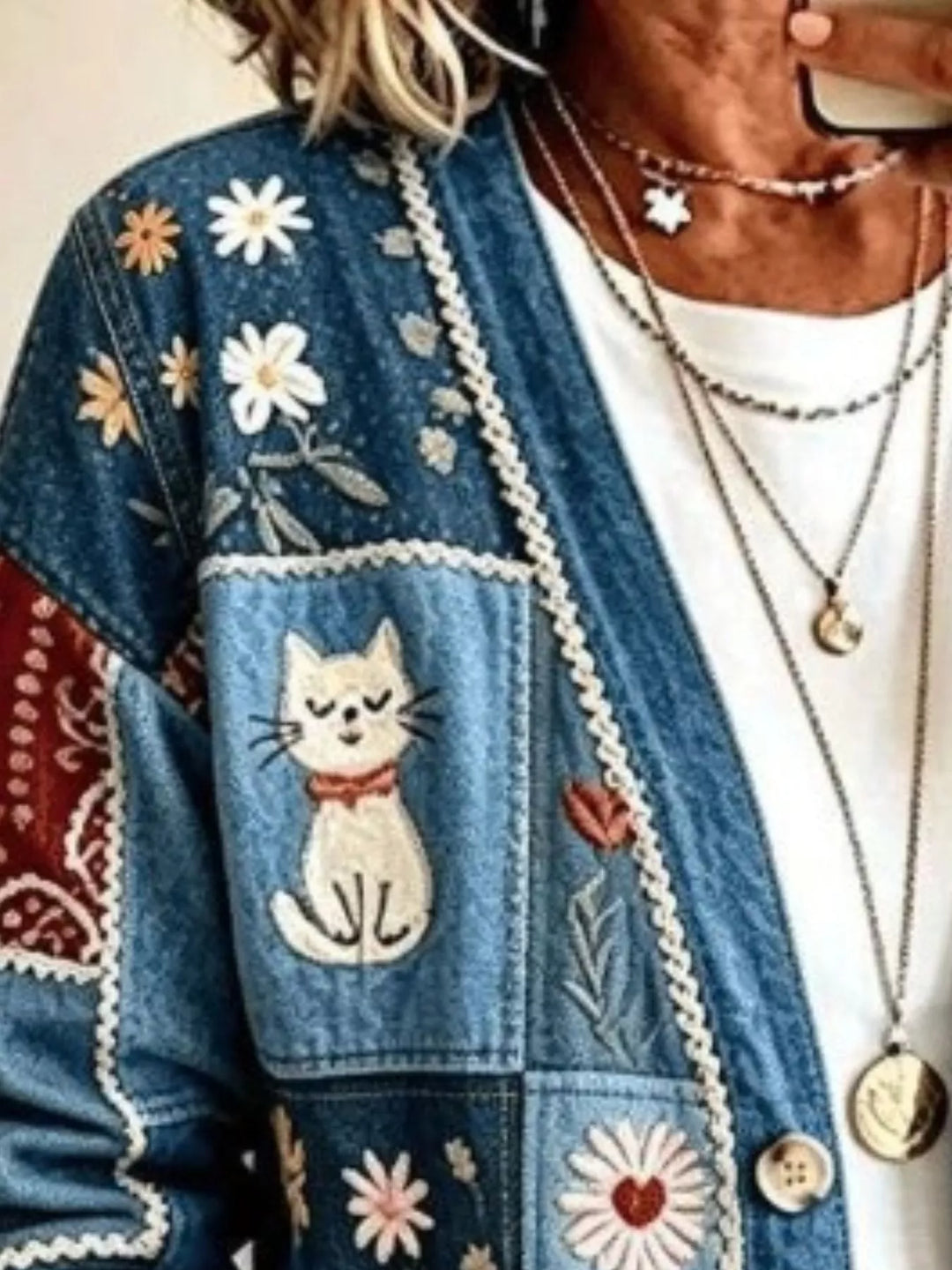 Close-up of denim blue cardigan cat embroidery and daisy patches