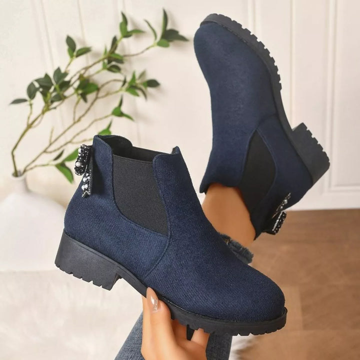 Navy block heel Chelsea boots held up, pair view with pearl bow