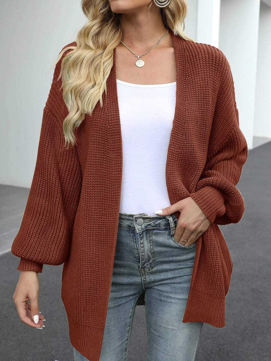 Rust chunky knit cardigan worn open over a white tank and jeans