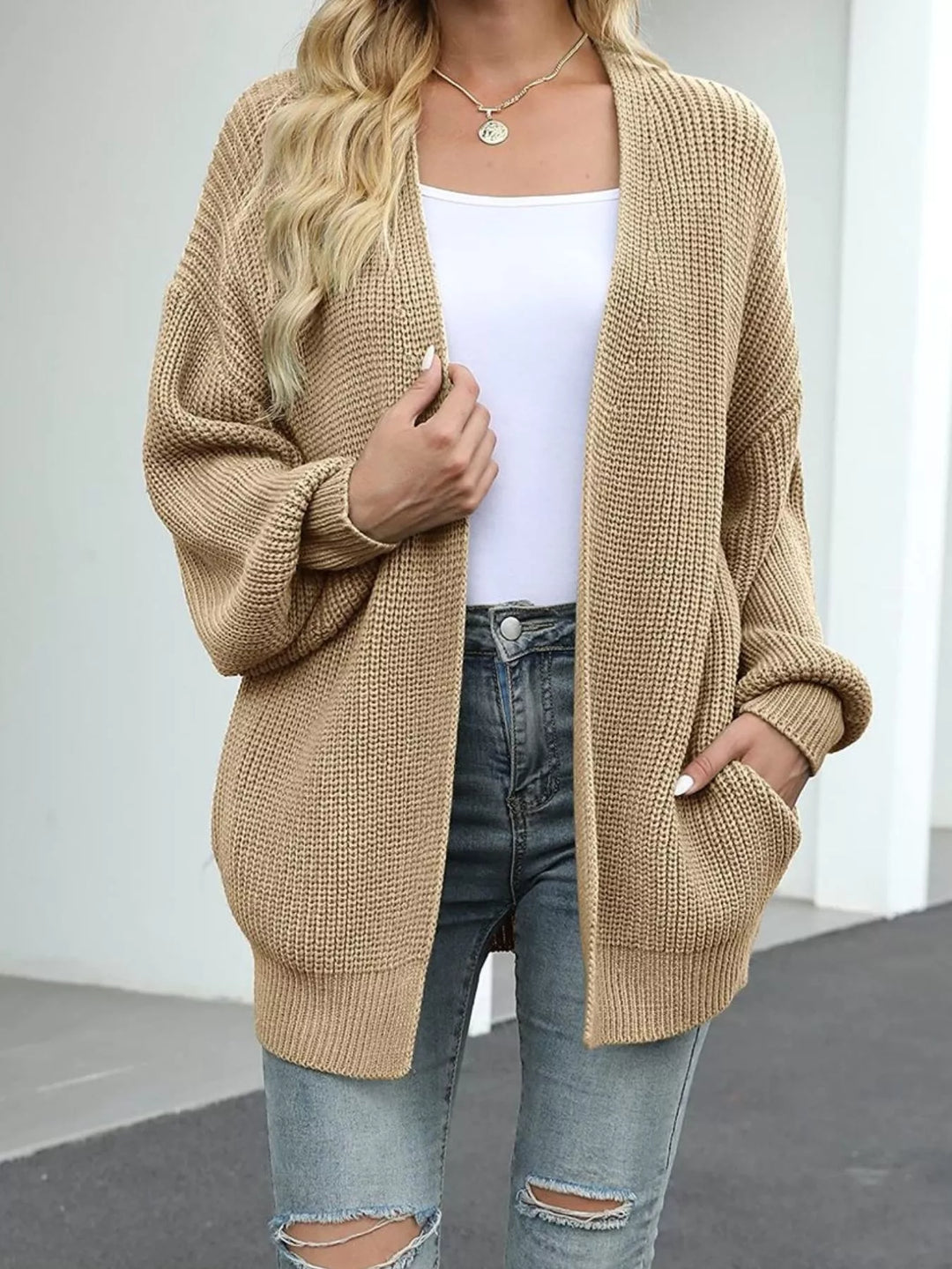 Tan chunky knit cardigan worn open with a hand in the pocket and ripped jeans