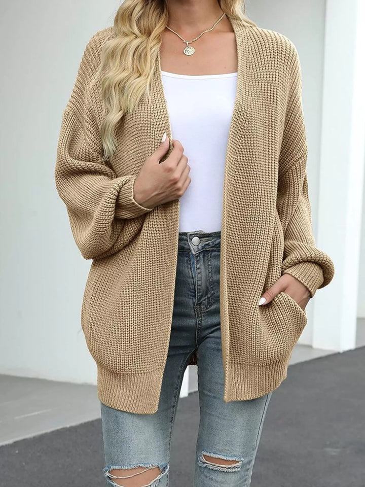 Tan chunky knit cardigan worn open with a hand in the pocket and ripped jeans