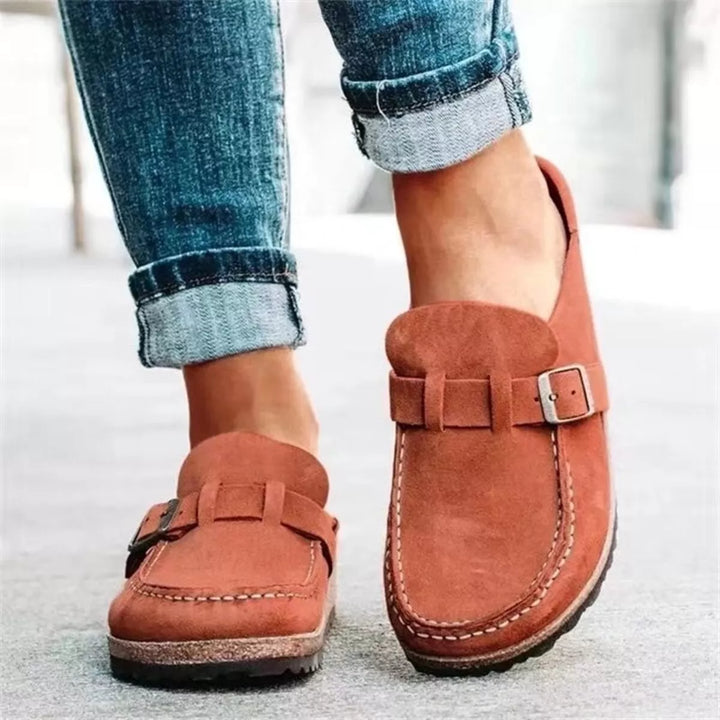 Rust slip on clogs with buckle strap worn with cuffed jeans, front view