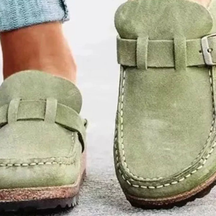 Close-up of sage green slip on clogs with buckle strap and stitched toe