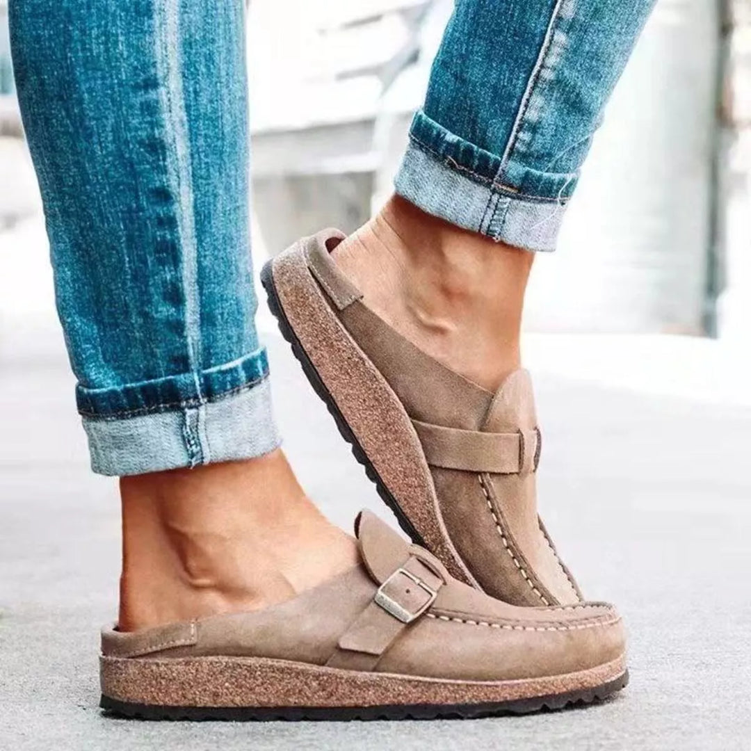 Taupe clog worn mid step, showing the buckle strap and cork-look footbed