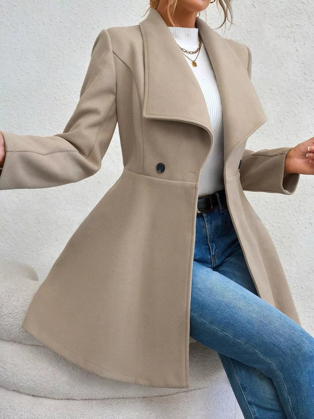 Beige double breasted coat worn open, seated pose with blue jeans