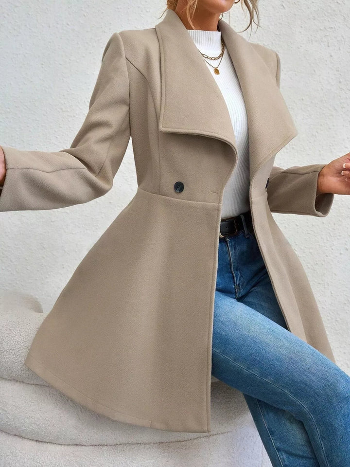 Beige double breasted coat worn open, seated pose with blue jeans