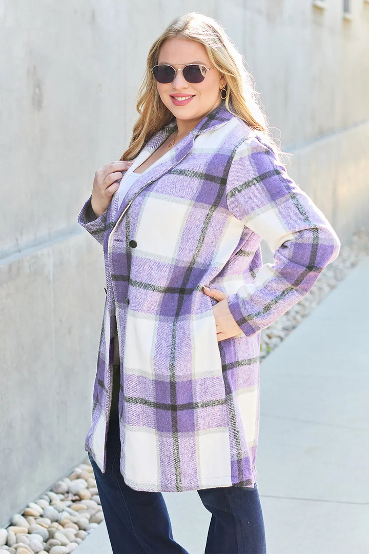 Lavender plaid coat worn with hands on hips against a concrete wall