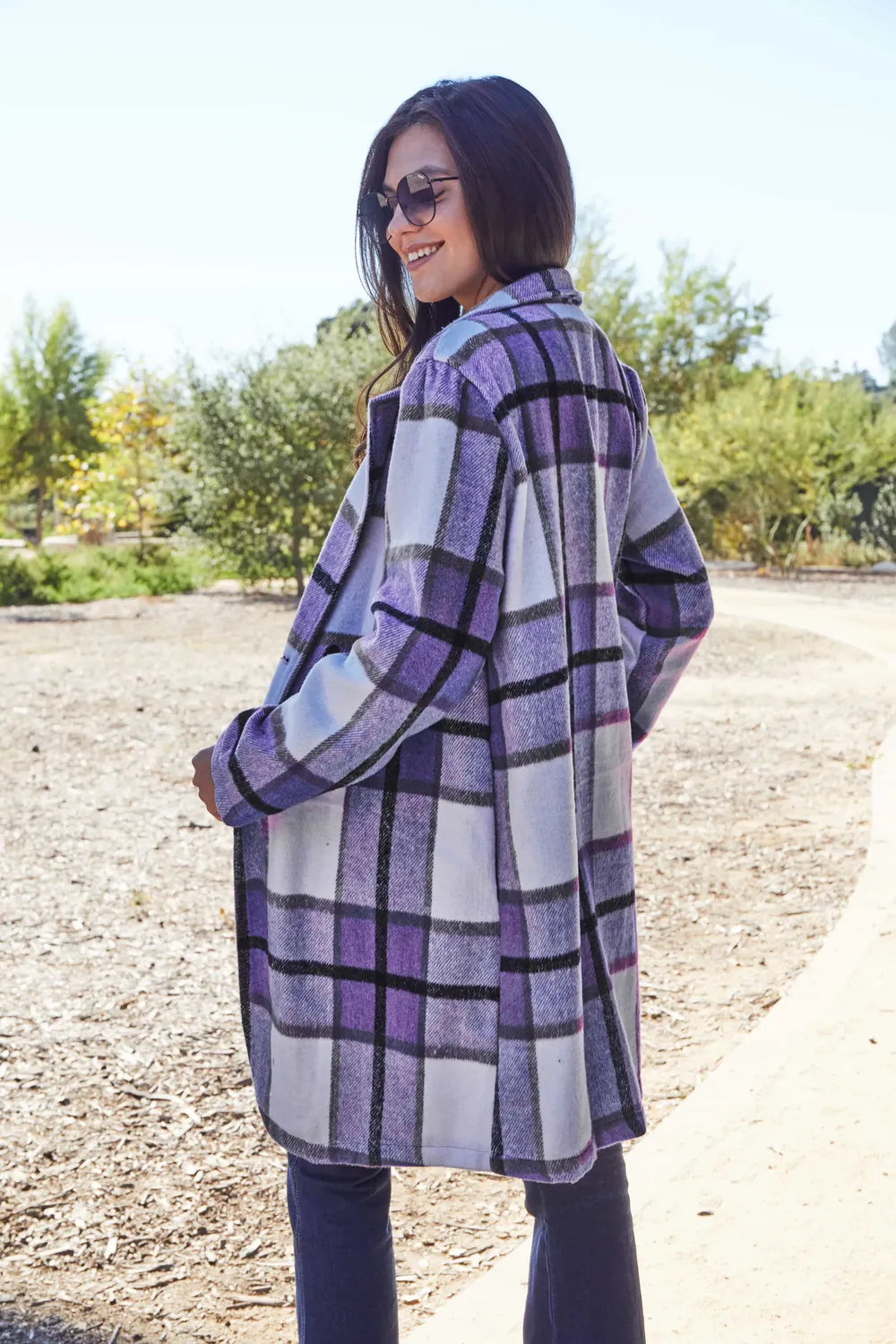 Lavender plaid coat side view with hand in pocket in a sunny park