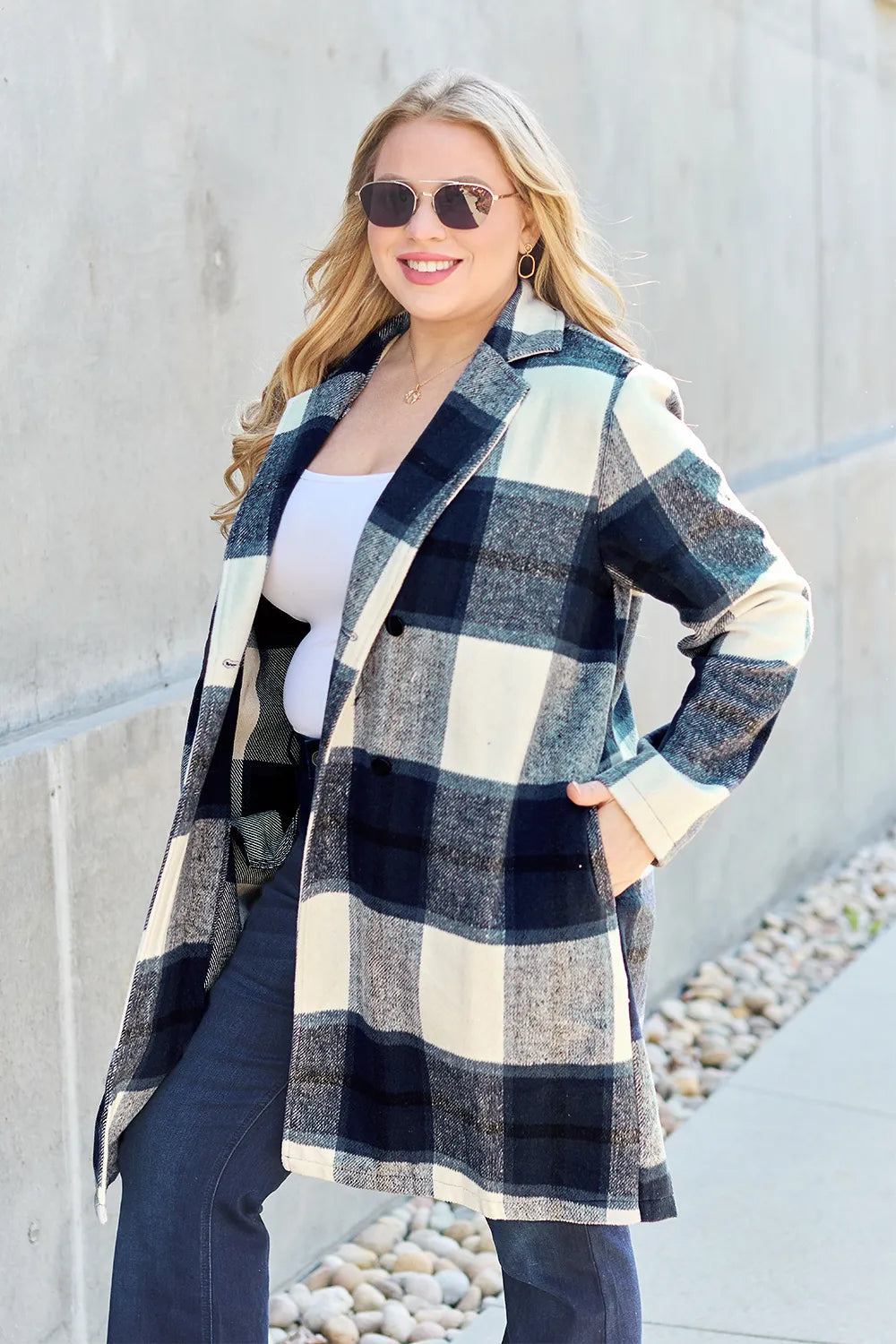 Navy plaid coat with sunglasses, worn open over jeans against a concrete wall