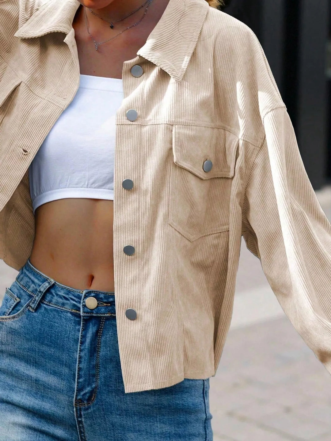 Beige cropped jacket over a white top, close-up of buttons and pocket