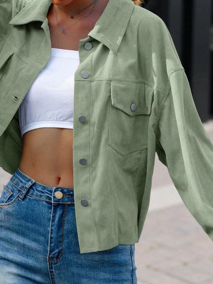 Sage green cropped jacket open over a white top, detail of the front
