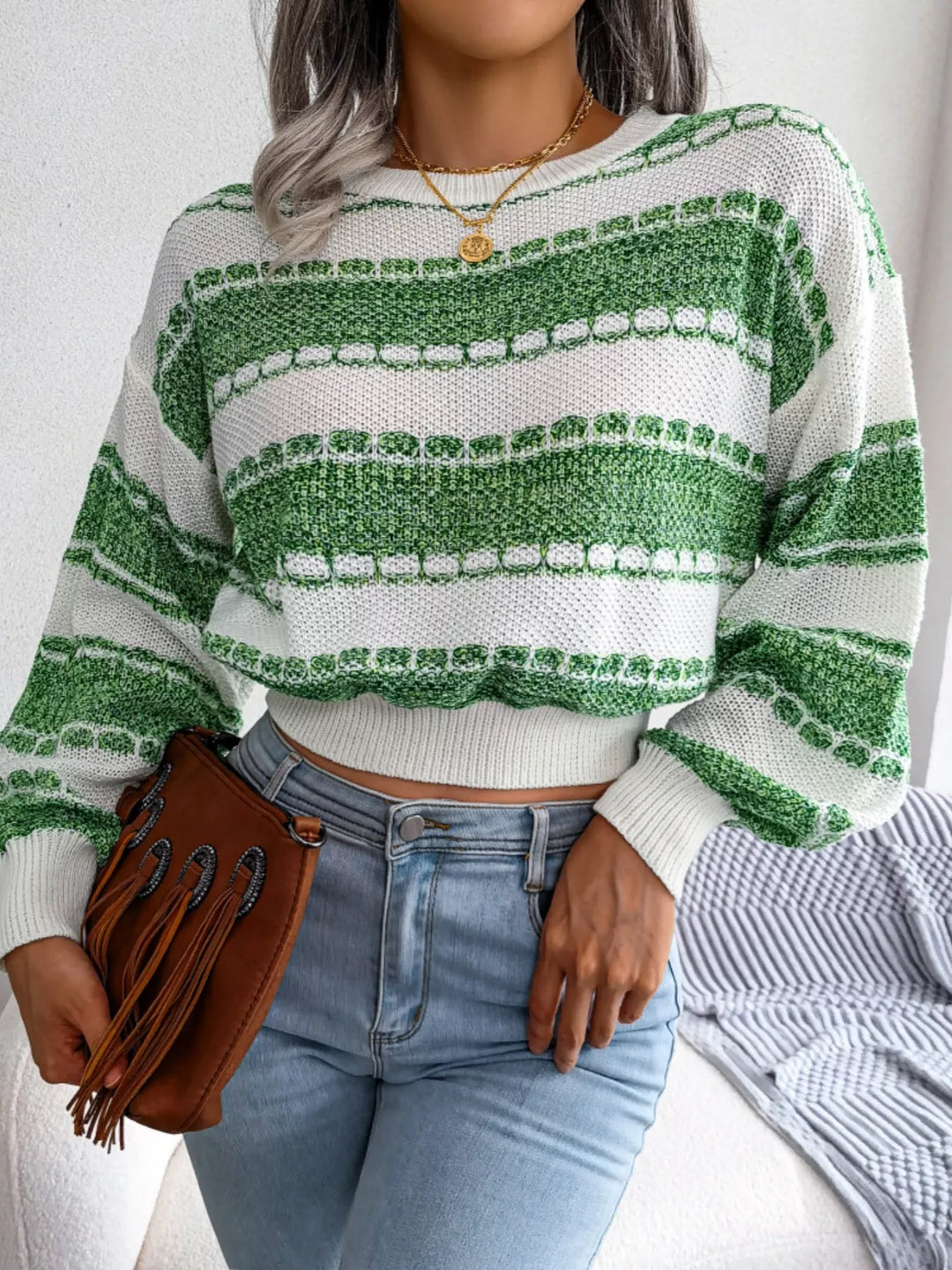 Green striped sweater with ribbed cuffs and a fringe clutch, standing