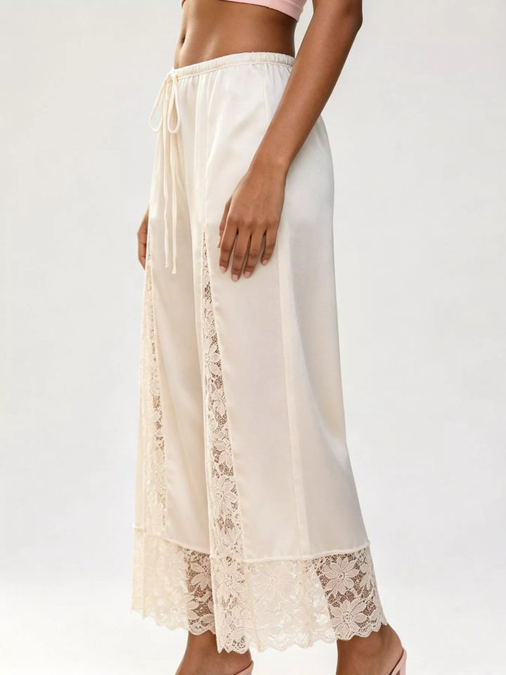 Side view of the ivory satin look pants with a lace trimmed hem