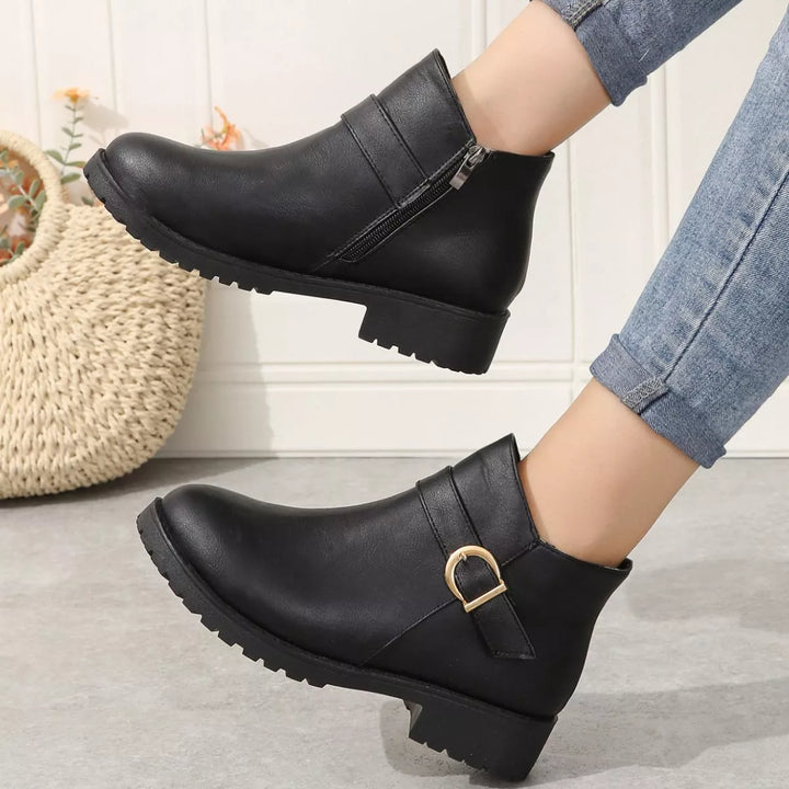 Black ankle boots with side zipper worn walking, one foot lifted