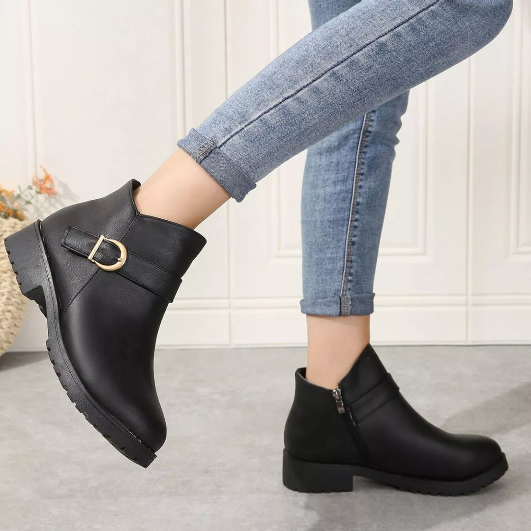 Black low block heel boots seen from the side with buckle detail while stepping