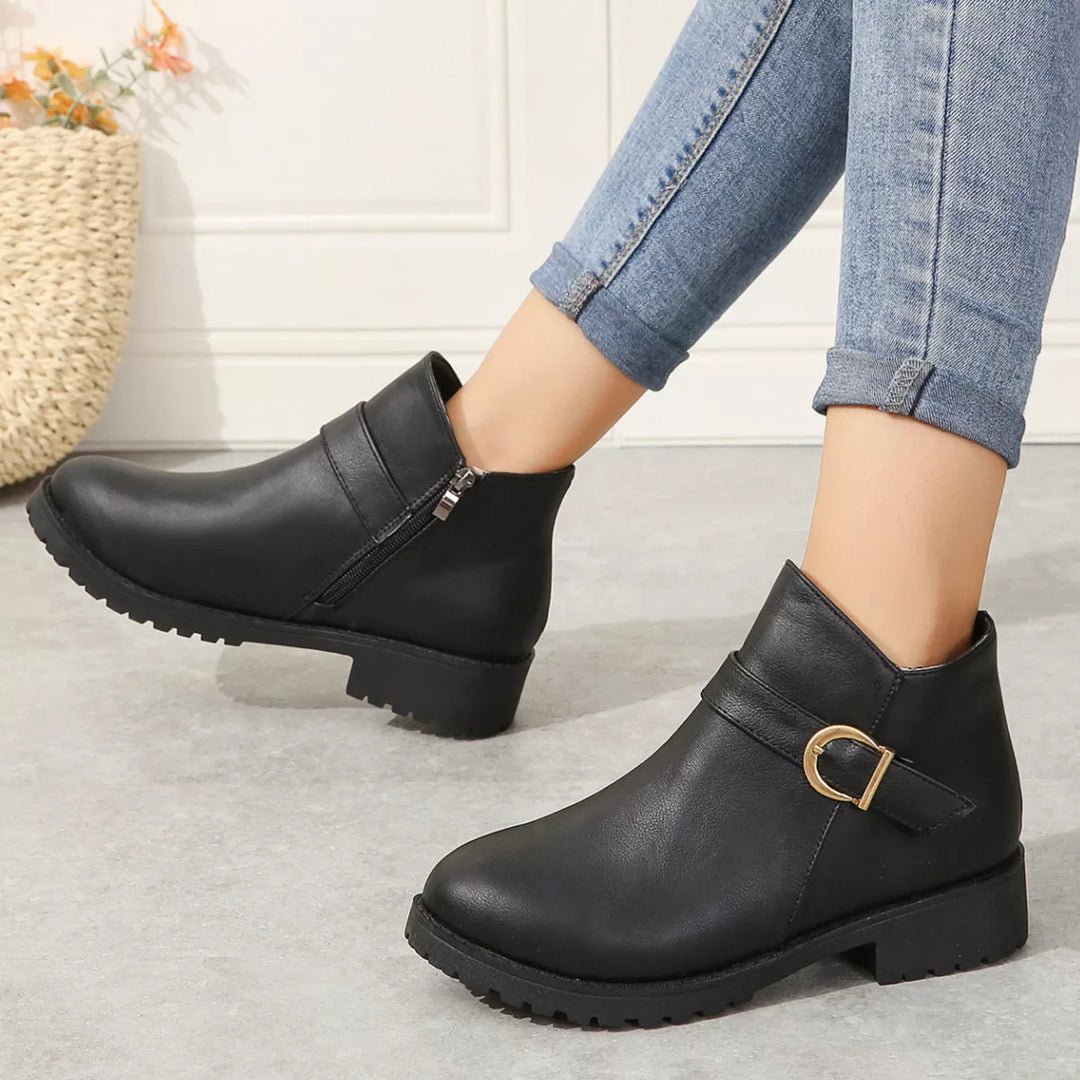 Women's fall boots in black with gold buckle strap, side view on feet with jeans