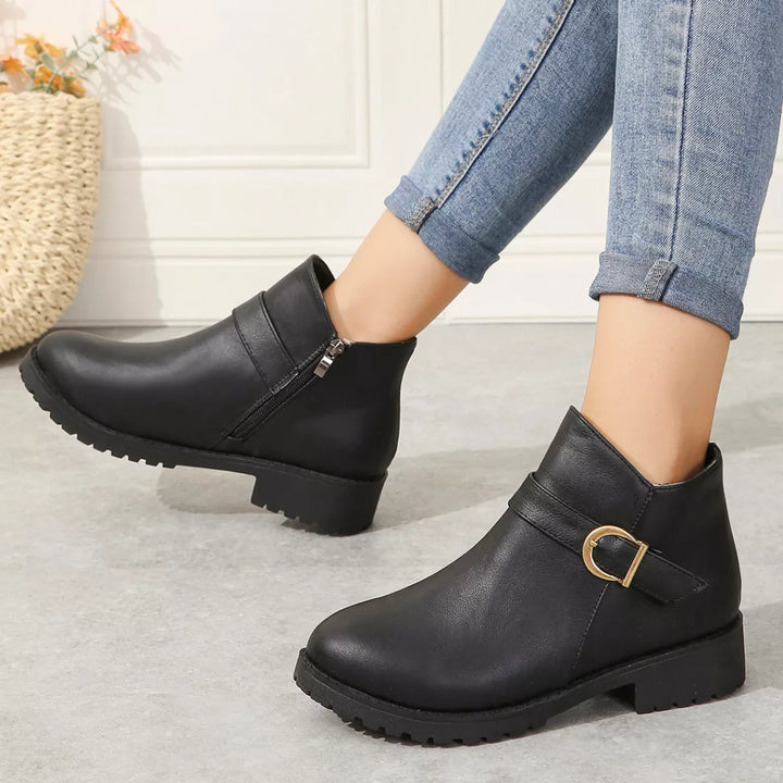 Women's fall boots in black with gold buckle strap, side view on feet with jeans