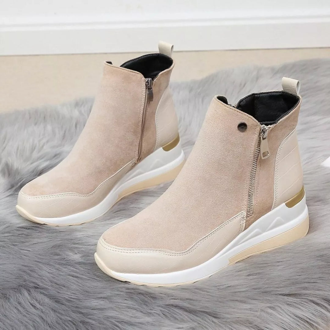 Pair of beige wedge boots with gold zipper pull on a gray rug